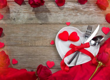 Kalp şeklinde tabak, kırmızı masa örtüsü ve güller masada.