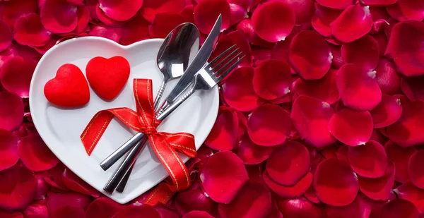 Rose petals on heart shaped plate and knife with fork — ストック写真