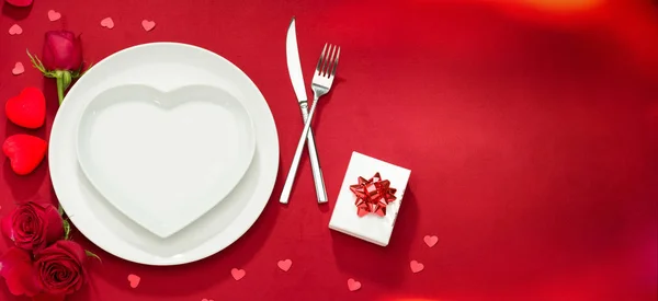 Placa, tenedor, cuchillo y rosas en la cubierta roja — Foto de Stock