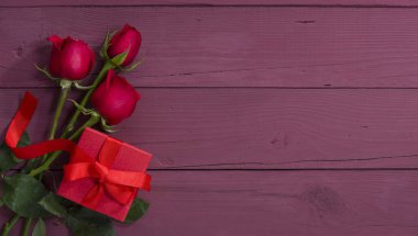 Renkli ahşap masada kırmızı hediye kutusu ve güller