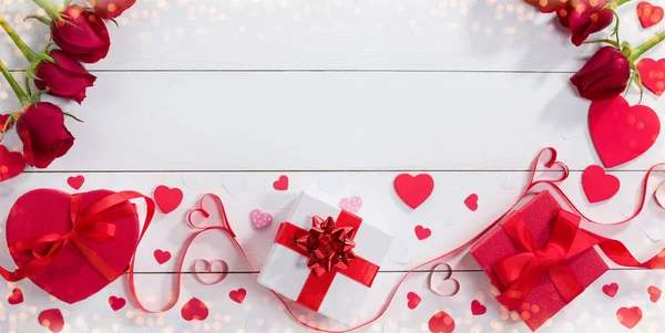 Подарочные коробки, ленточные сердечки и розы на белом столе . — стоковое фото