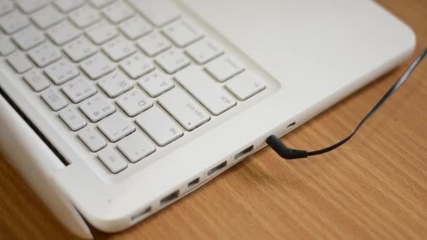 Una donna sta collegando il jack audio delle cuffie a un computer portatile bianco — Video Stock