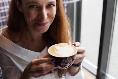 Genç bir kadın balkonda cappuccino içiyor.