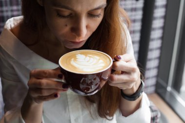 Pencerenin yanında kapuçino içen genç bir kadın.