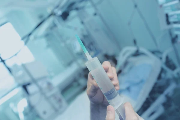 Full syringe on the background of patient's bed — Stock Photo, Image