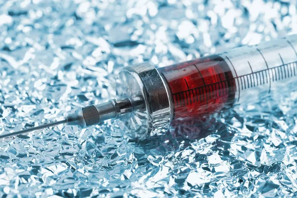 Old filled syringe on the crumpled metallic paper — Stock Photo, Image