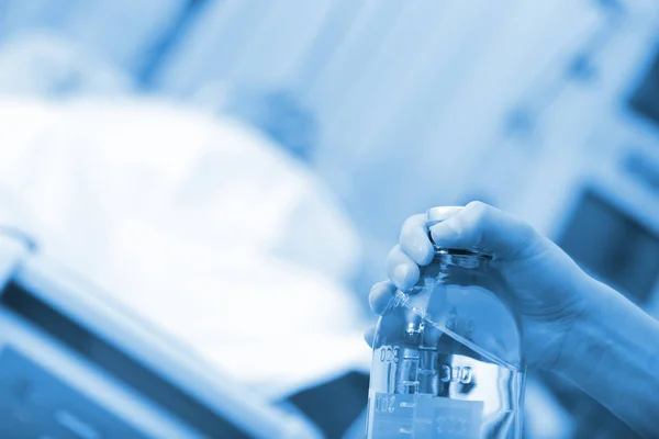 Kvinnlig sjuksköterska händer med saltlösning flaska på bakgrunden av sovande patient — Stockfoto