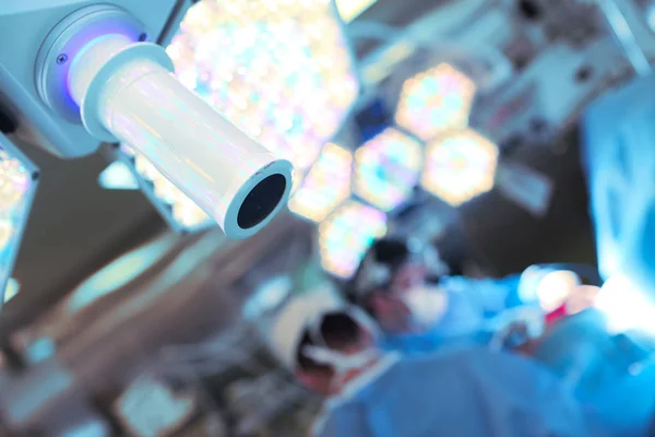 Blurred surgeons in the operating room and surgical lamp close-u — Stock Photo, Image