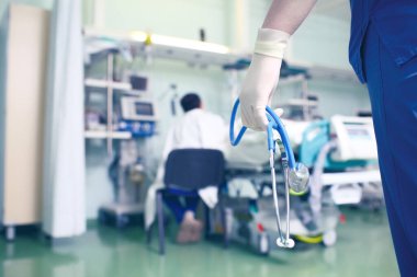 Elinde steteskop olan bir doktorun hastane koğuşunda hasta yatağının yanında oturan bir adamın arka planında ne işi var?.
