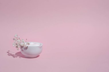 Havadar beyaz kremalı ve çiçekli kavanoz, doğal doku, pembe arka plan