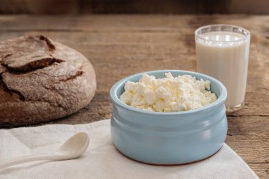 Kahvaltıda doğal süt ürünleri, mavi kasede süzme peynir, bir bardak süt, eski ahşap bir masada taze ev yapımı ekmek.