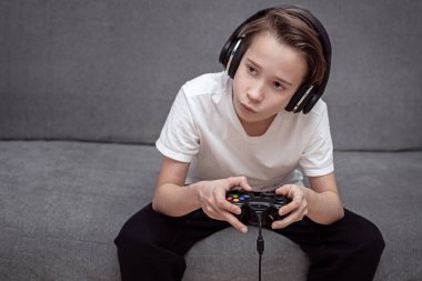 Bir çocuk evdeki kanepede oturuyor ve elinde bir joystick tutuyor, video oyunları oynuyor, bir oyun konsolu