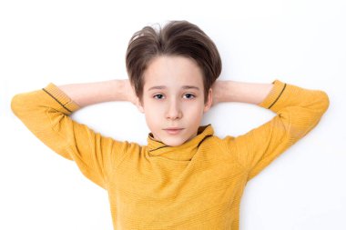 Sarı elbiseli bir çocuk beyaz arka planda yatıyor, elleri başının üstünde, bir genç dinleniyor.