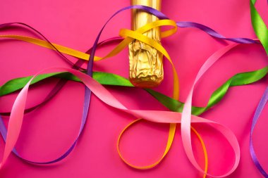 Şampanya şişesi boynu altın folyoyla ve parlak pembe arka planda renkli saten kurdeleler düz manzaralı. Kutlama ve kutlama kavramı, doğum günü, tebrikler, mutluluk, parti 