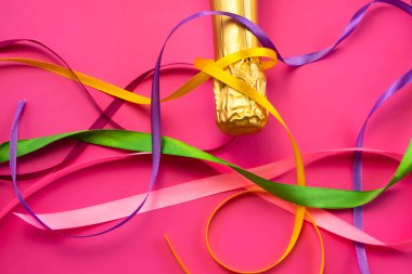 Şampanya şişesi boynu altın folyoyla ve parlak pembe arka planda renkli saten kurdeleler düz manzaralı. Kutlama ve kutlama kavramı, doğum günü, tebrikler, mutluluk, parti 