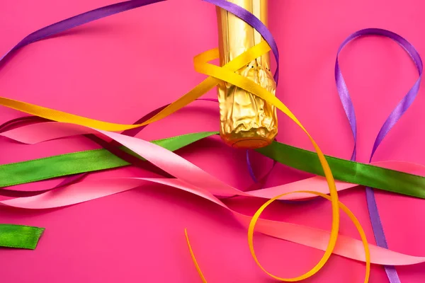 Şampanya şişesi boynu altın folyoyla ve parlak pembe arka planda renkli saten kurdeleler düz manzaralı. Kutlama ve kutlama kavramı, doğum günü, tebrikler, mutluluk, parti 