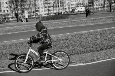 Saint-Petersburg, Rusya - 3 Mart 2020: Terkedilmiş boş bir parkta bisiklet süren küçük bir kız bisiklet yolu üzerinde, arka planda tuğladan apartmanlar, şehir manzarası, siyah beyaz fotoğraf, yalnızlık
