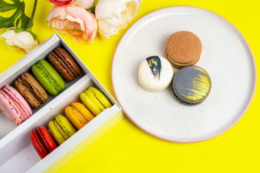 Sarı renkte romantik bir doğum günü kutlaması için hediye kutundaki renkli badem kurabiyeleri, pion çiçekleri, saten kurdele üst görünümü, birçok farklı türde makaron çeşitleri elle süslenmiş altın gümüşler.