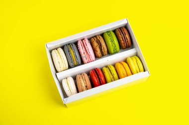 Sarı renkte romantik bir doğum günü kutlaması için hediye kutundaki renkli badem kurabiyeleri, pion çiçekleri, saten kurdele üst görünümü, birçok farklı türde makaron çeşitleri elle süslenmiş altın gümüşler.