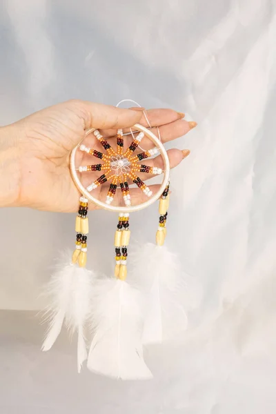 Dream catcher in female woman hand on satin, handmade native american of yellow blue beads with white feathers. Bad dreams protection. Concept peaceful, peace of mind, meditation, tranquility