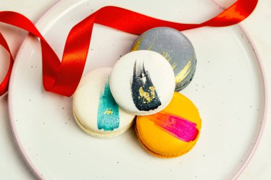 Tabaktaki renkli, modern, muhteşem badem kurabiyeleri romantik parti yıldönümleri için beyaz, pion çiçekleri, saten kurdele üst görünümü, birçok farklı türde makaron çeşitleri el yapımı altın gümüş süslemeler.