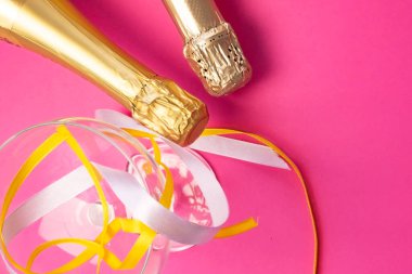 İki şampanya şişesi altın folyoyla boynu, şampanya bardağının yanında ve parlak pembe, düz manzaralı renkli saten kurdeleler. Kutlama konsepti, doğum günü, tebrikler, mutluluk, parti