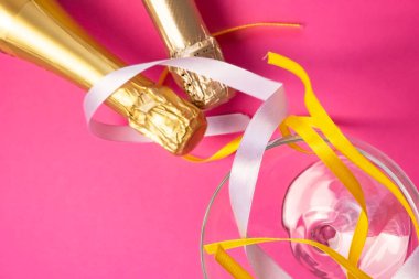 İki şampanya şişesi altın folyoyla boynu, şampanya bardağının yanında ve parlak pembe, düz manzaralı renkli saten kurdeleler. Kutlama konsepti, doğum günü, tebrikler, mutluluk, parti