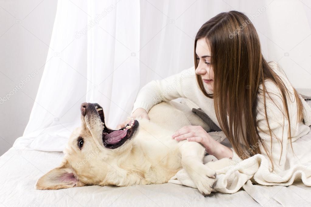 Girl playing with her dog labrador retriever in a bed