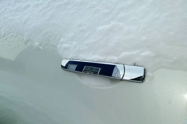 Nickel door handle on a white car door and snow. In the pen is a reflection of the building. Side view.