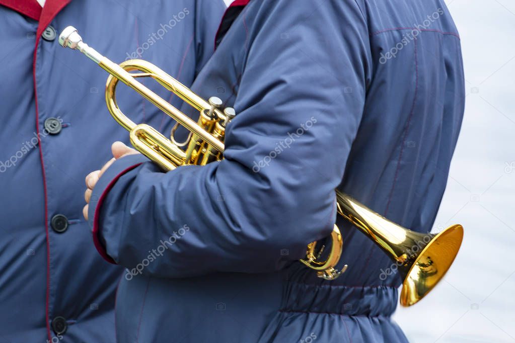 Two men are standing in blue cloaks. One of them has wind musical instrument -  trumpet under arm. Side view.