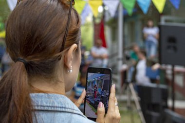 Kahverengi saçlı kız akıllı telefondan sokak müziği performansı sergiliyor. Arkadan bak. Surgut, Rusya - 12 Eylül 2019.