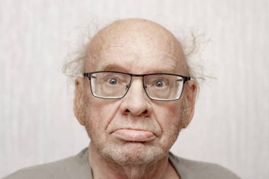 Gri elbiseli, saç stili olmayan yaşlı bir adam kameraya bakıyor. Portreyi kapat. Boyut olarak. Ön manzara. Kavram.