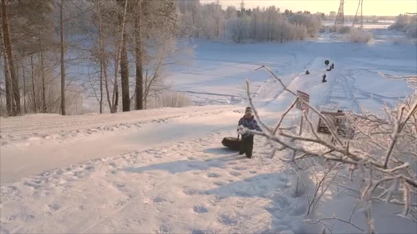 子供は雪の丘を登ってチューブをドラッグしますロシアのサーグート 2019年12月25日 — ストック動画