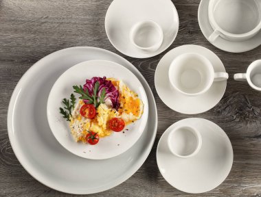 Çırpılmış yumurta, domates ve otlarla ahşap bir arka planda beyaz bir tabakta.