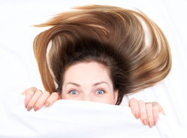 Amazing girl with open eyes looking out from under the covers