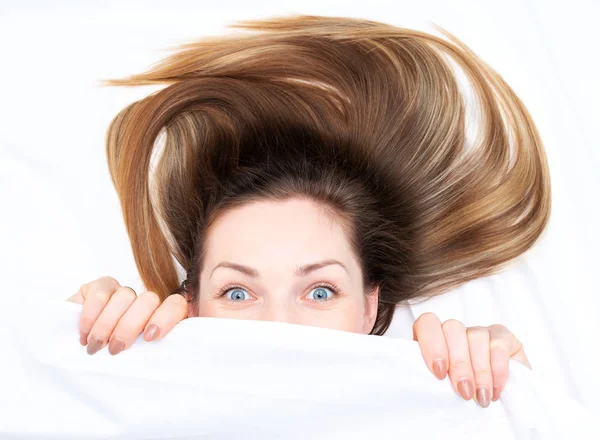 Verbazingwekkend meisje met open ogen kijken uit van onder de dekens — Stockfoto