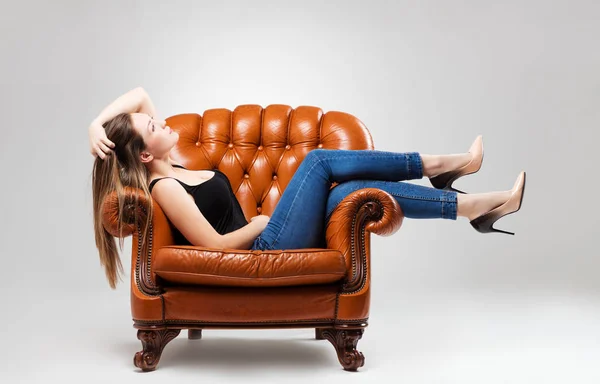 Een jong meisje poseren voor de camera in jeans terwijl ze op een stoel zit — Stockfoto