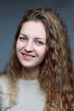 Kameranın önünde kıvırcık saçlı genç bir kadın poz veriyor.