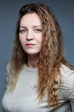 Kameranın önünde kıvırcık saçlı genç bir kadın poz veriyor.