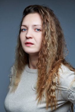 Kameranın önünde kıvırcık saçlı genç bir kadın poz veriyor.