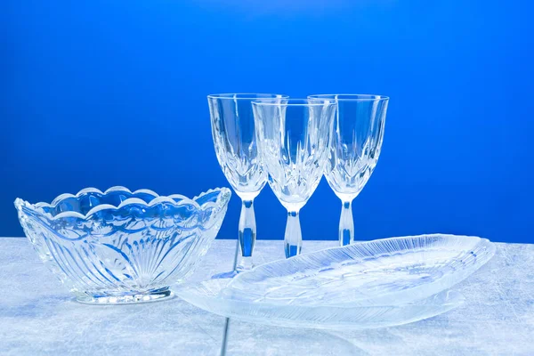 Drei Kristallgläser und Geschirr mit Nahaufnahme auf blauem Hintergrund — Stockfoto