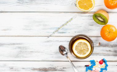 Çay, limon, termometre, vitamin ve grip tedavisi için haplar. Tahta beyaz arka planda