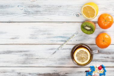 Çay, limon, termometre, vitamin ve grip tedavisi için haplar. Tahta beyaz arka planda