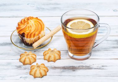 Tahta arka planda bir dilim limonlu ve kurabiyeli çay..
