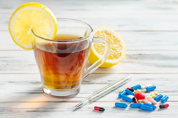 Çay, limon, termometre, vitamin ve grip tedavisi için haplar. Tahta beyaz arka planda