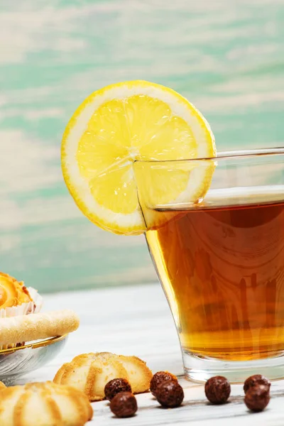 Чашка горячего чая с лимоном и печеньем на белом деревянном фоне . — стоковое фото