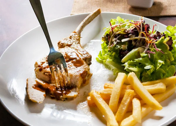Hand using knife cutting grilled pork chops steak Close up in restaurant, Pork chop steak with salad and french fries