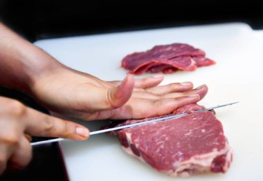 İşteki şef, yemek pişirmek için dilimlenmiş domuz eti, plastik bir tahtada bıçakla domuz eti kesme.