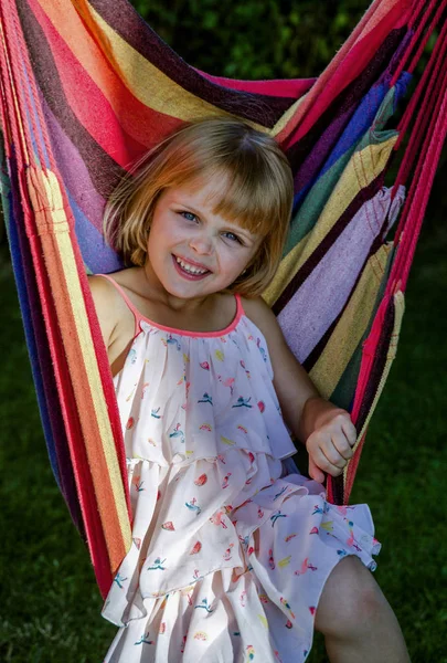 Menina bonito encontra-se em uma rede ao ar livre, tem um descanso no jardim . — Fotografia de Stock