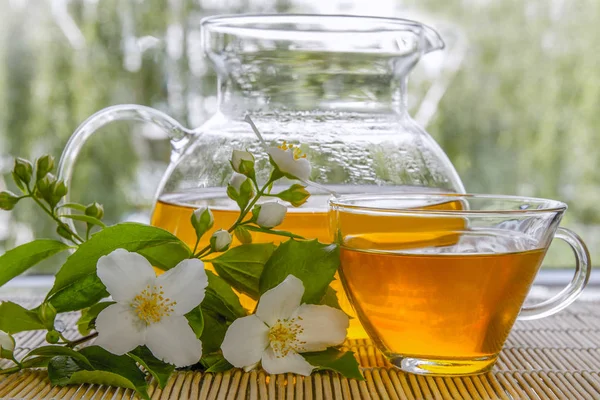 Yasemin Yeşil çay bir cam çaydanlık ve bambu hasır üzerinde taze Yasemin çiçekleri. Yakın çekim. 